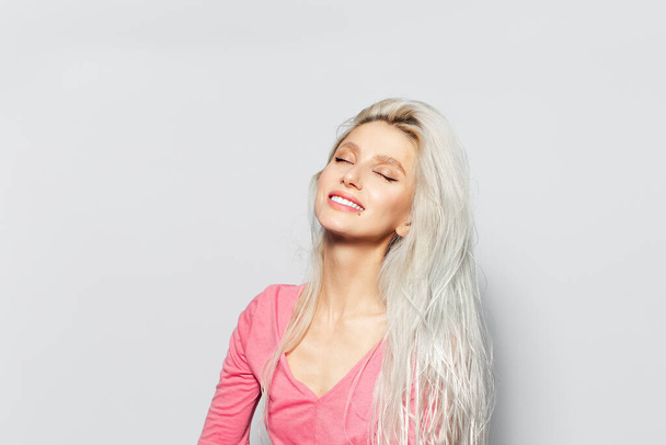 Studio portrét mladé krásné usměvavé dívky s blond vlasy v růžové košili na bílém pozadí. - Fotografie, Obrázek