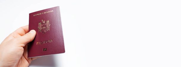Großaufnahme einer männlichen Hand, die einen moldawischen Pass mit roter Farbe an einer weißen Wand hält. Panorama-Banner mit Kopierraum. - Foto, Bild