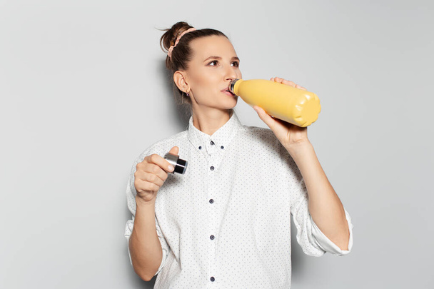 Retrato de estudio de una joven sonriente, bebiendo agua de la botella termo de color amarillo sobre fondo blanco. Concepto de salud. - Foto, Imagen