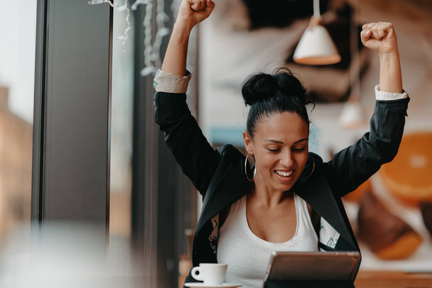 A woman sits in a cafe with her arms raised and celebrating a job well done. Business concept. High quality photo - Fotó, kép