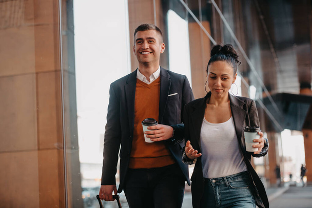 Business man and business woman talking and holding luggage traveling on a business trip, carrying fresh coffee in their hands.Business concept. High quality photo - Φωτογραφία, εικόνα