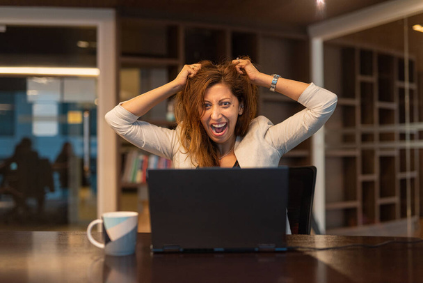 Mujer enojada y frustrada usando computadora portátil en la oficina tiro horizontal - Foto, imagen