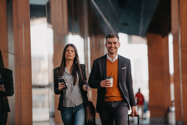 Business man and business woman talking and holding luggage traveling on a business trip, carrying fresh coffee in their hands.Business concept. High quality photo - Photo, Image