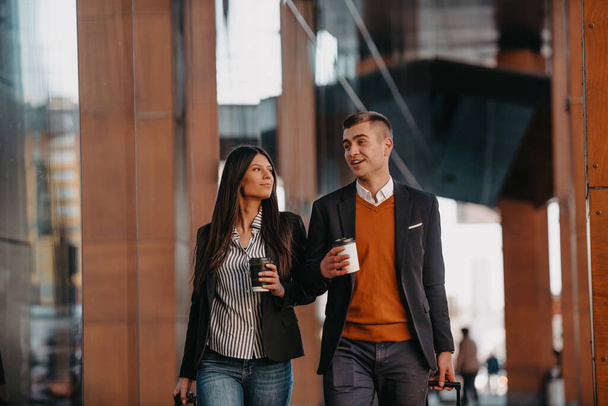 Business man and business woman talking and holding luggage traveling on a business trip, carrying fresh coffee in their hands.Business concept. High quality photo - Zdjęcie, obraz