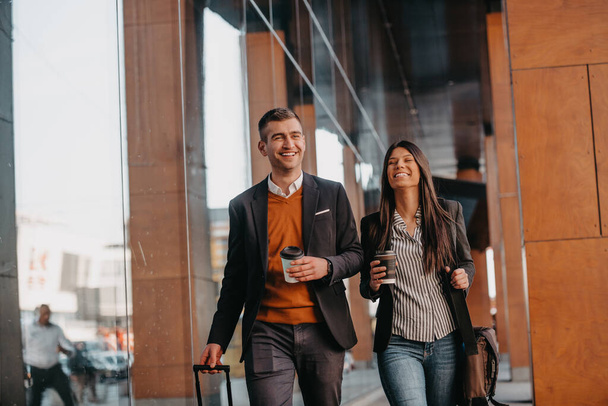 Business man and business woman talking and holding luggage traveling on a business trip, carrying fresh coffee in their hands.Business concept. High quality photo - Valokuva, kuva