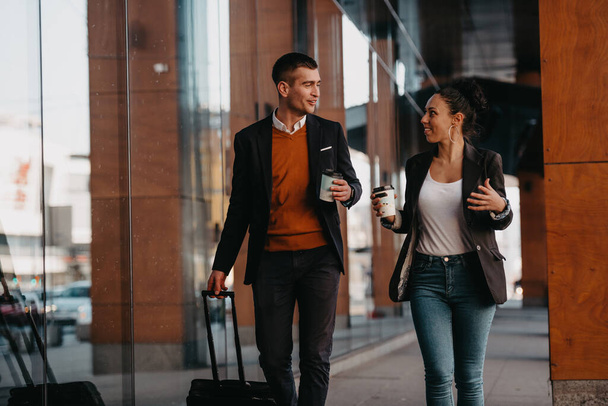 Business man and business woman talking and holding luggage traveling on a business trip, carrying fresh coffee in their hands.Business concept. High quality photo - Foto, afbeelding