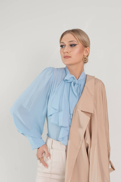Vertical attractive, confident blond businesswoman in formal stylish outfit with jacket on shoulder posing on white studio background. Fashionable clothes collection and magazine advertisement - Fotó, kép