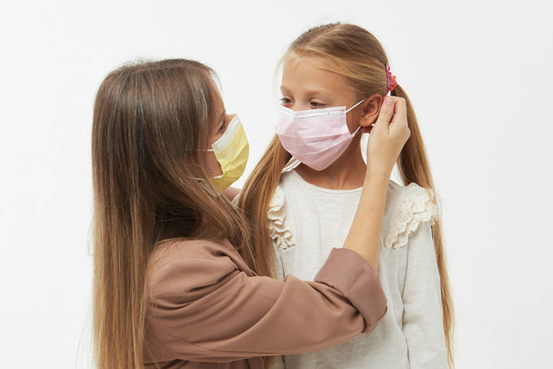 Caring for loved ones. Young mother hugs little daughter in protective medical masks during Covid-19 pandemics. Studio white background - Fotó, kép