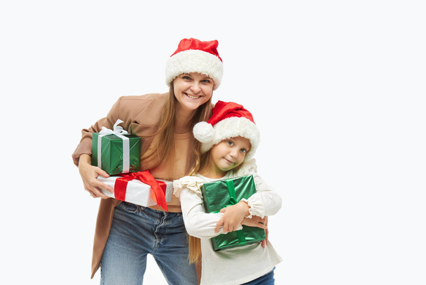 Christmas family. Cute young mother and daughter in santa Claus caps holding colorful gift boxes on white. Preparing for New Year's holidays in Italy - Foto, afbeelding
