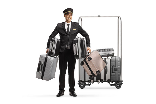 Bellboy in possesso di molte valigie e in piedi di fronte a un carrello bagagli hotel isolato su sfondo bianco - Foto, immagini