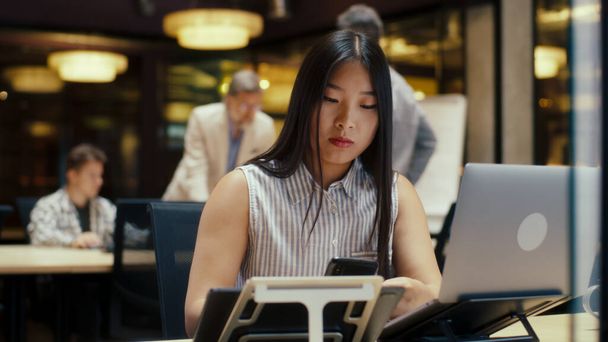 Mujer asiática que trabaja en el proyecto de negocios en la oficina moderna cerca de compañeros de trabajo utilizando el ordenador portátil y teléfono inteligente. Empresa de comercialización de comercio electrónico - Foto, Imagen
