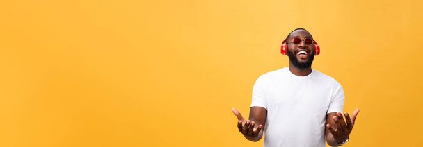 Przystojny młody mężczyzna African American słuchania i uśmiechając się z muzyką na swoim urządzeniu przenośnym. Na białym tle nad żółtym tle - Zdjęcie, obraz