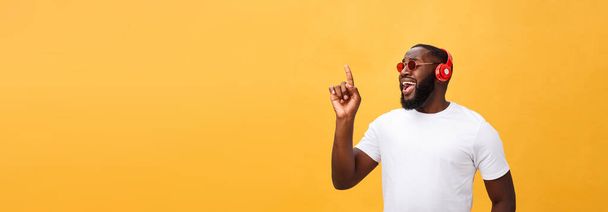 Handsome young African American man listening and smiling with music on his mobile device. Isolated over yellow background - Fotografie, Obrázek