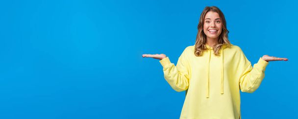 Carefree happy smiling woman weighing something in arms, as if holding two products, look camera suggest make choice, deciding between variants, stand blue background. - Photo, Image