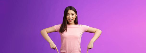 Lebhaft enthusiastisch asiatische Brünette weiblich begeistert erzählt von super Promo, zeigt überrascht nach unten, grinst freudig empfehlen gute Werbung, zeigt unten Werbung. - Foto, Bild
