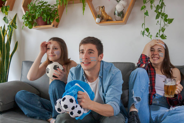 Три молодых аргентинских друга, две девочки и мальчик, смотрящий футбол, разочарованный и отчаявшийся. - Фото, изображение