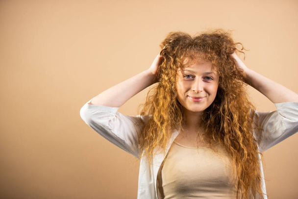 Portrait of smiling redhead pretty young woman posing for the camera holding her hands on hair and straightens them. . High quality photo - Φωτογραφία, εικόνα