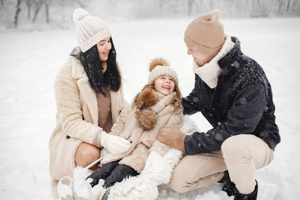 Little girl, father and mother playing outdoors at winter day. Brunette young woman, man and little girl in winter in warm jackets walk in the park with a sled. Mother and daughter wearing winter - Fotoğraf, Görsel