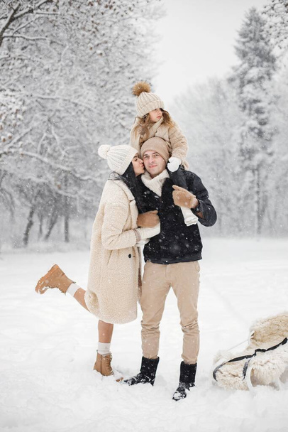 Little girl, father and mother playing outdoors at winter day. Brunette young woman, man and little girl in winter in warm jackets walk in the park with a sled. Mother and daughter wearing winter - Foto, Imagen