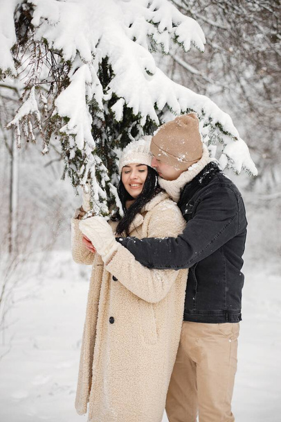 Young man and woman hugging and kissing outdoors. Romantic couple at winter in warm jackets walk in the park and hugging. Man and woman wearing winter clothes and knitted hats. - Foto, imagen
