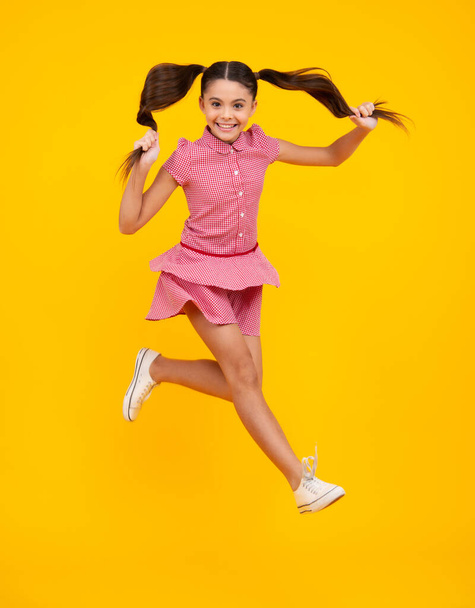 Excited teenager. Full length funny teenager kid jump enjoy rejoice win isolated on yellow background. Small child girl in dress jumping - Foto, Bild