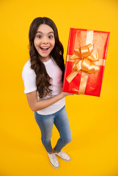 Amazed teenager. Child with gift present box on isolated studio background. Gifting for kids birthday. Excited teen girl - Foto, Imagem