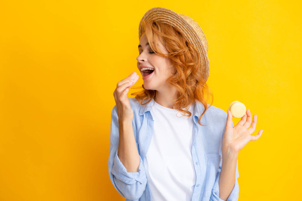 Leuke jonge vrouw met makaron. Mooi glimlachend jong meisje eten kleurrijke ara 's over gele achtergrond - Foto, afbeelding