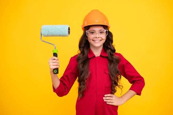 Painter in workshop. Renovation and repair. Teen girl in helmet with painting brush. Child in hard hat. Kid builder painter on construction site. Happy positive and smiling emotions of teenager girl - Photo, Image