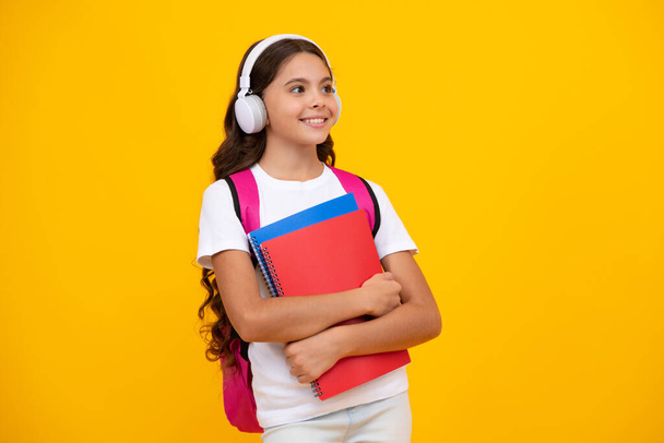 Schoolchild, teenage student girl with headphones and school bag backpack on yellow isolated studio background. Children school and education concept - Foto, Imagem