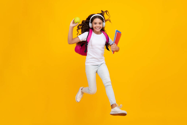 Zpátky do školy. Teenager školní dívka s batohem a sluchátky držet knihy připravené učit. Školní děti na izolovaném žlutém pozadí studia - Fotografie, Obrázek