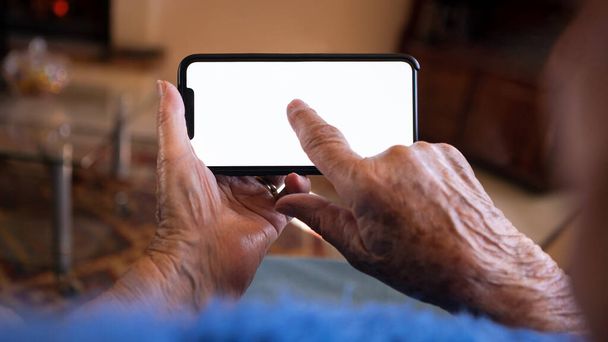 Zmarszczone ręce starej kobiety trzyma smartfon z białym, pustym ekranem do makiety. Zamknij starsze ręce białej babci pokazuje pusty telefon dla nowej aplikacji mobilnej lub stronie internetowej. - Zdjęcie, obraz
