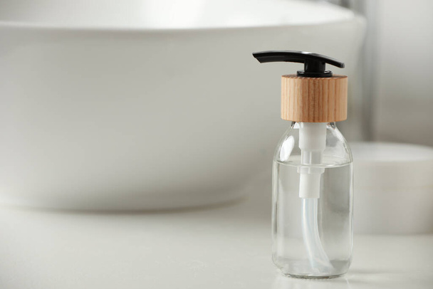 Bottle with dispenser cap on white table in bathroom, closeup. Space for text - Photo, Image