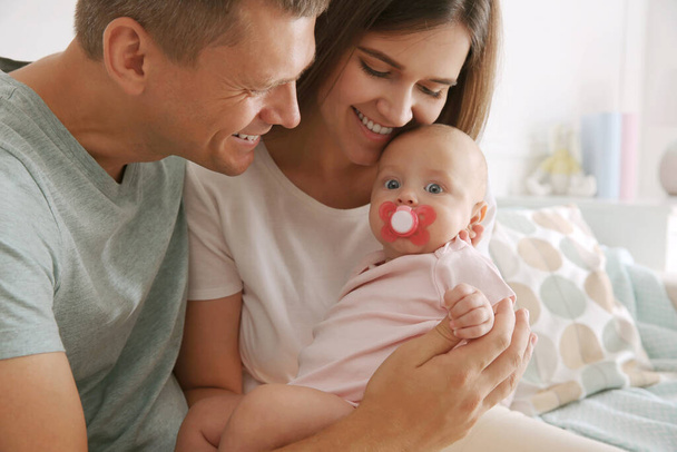Happy couple holding their cute little baby with pacifier at home - Фото, изображение