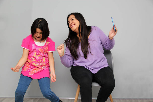 Hispanic Latino mom and daughter play, dance, surprise, enjoy, taking selfies using the cell phone spending quality family time - Photo, Image