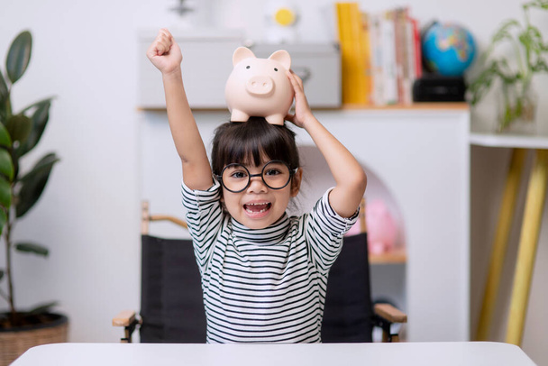 Little Asian girl saving money in a piggy bank, learning about saving, Kid save money for future education. Money, finances, insurance, and people concept - Foto, imagen
