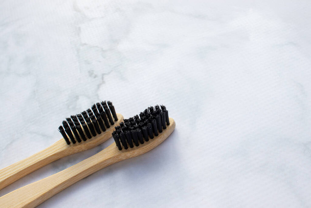 Natural bamboo toothbrush with black bristles on white marble table in bathroom. Top view, copy space. Zero waste, reusable, sustainable, eco friendly tooth brush - Foto, Imagem