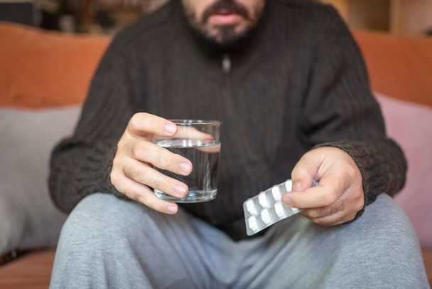 Sick man holding a pack of pills and a glass of water to drink - Foto, afbeelding