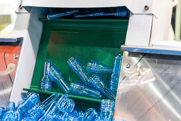 molte materie prime trasparenti per animali domestici in plastica blu preformate in secchio metallico durante il trasporto tramite trasportatore a gradini inclinato al processo di produzione automatico bottiglia d'acqua che soffia nell'industria delle bevande - Foto, immagini