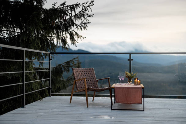 Spacious terrace with cozy table and chair highly in mountains at dusk. Cozy lounge place for rest at house on nature - Photo, Image