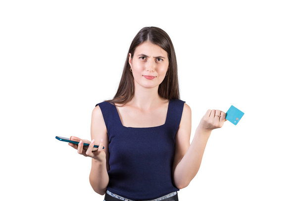 Недовольная молодая женщина выглядит смущенной, держа в руках смартфон и кредитную карту, изолированную на белом фоне с копировальным пространством. Проблемы и трудности мобильного банкинга в Интернете - Фото, изображение