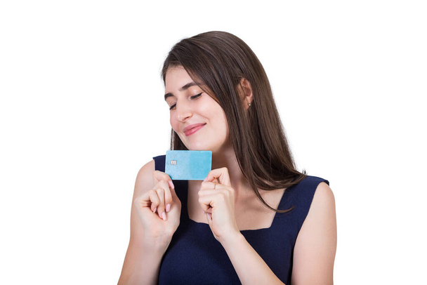 Overjoyed young woman holding to chest her favorite credit card. Close up portrait of a dreamy girl with eyes closed wishing for sale and discounts isolated on white background with copy space - Photo, Image