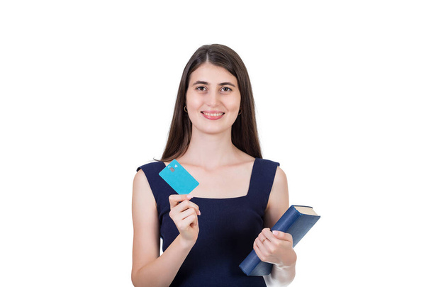 Vidám diáklány kezében egy könyv és egy hitelkártya, látszó elégedett kamera elszigetelt fehér háttérrel fénymásolás hely - Fotó, kép