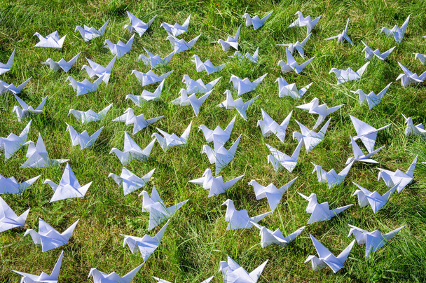 Japán hajtogatott Origami daruk friss füvön. Több száz kézzel készített papírmadár a zöld mezőn, fénymásolási hellyel. 1000 ezer daru tsuru szobor téma. A béke, a hit, az egészség, a kívánságok és a remény szimbóluma  - Fotó, kép