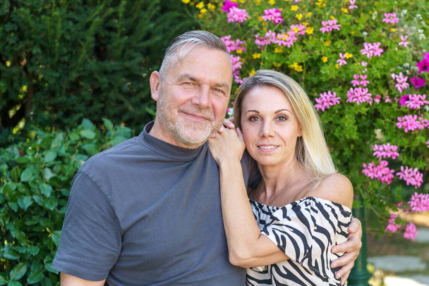 Feliz pareja de mediana edad posando brazo en brazo en un amoroso retrato familiar al aire libre en un jardín de verano - Foto, imagen