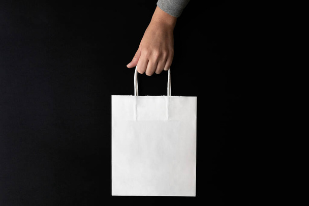 Hand carrying a white shopping bag over a black background, left hand - Photo, image
