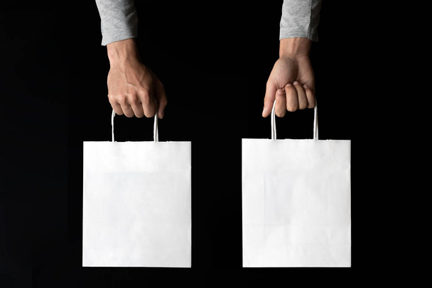 Dvě ruce na obou stranách drží bílou papírovou tašku nad černým pozadím pro napodobení - Fotografie, Obrázek