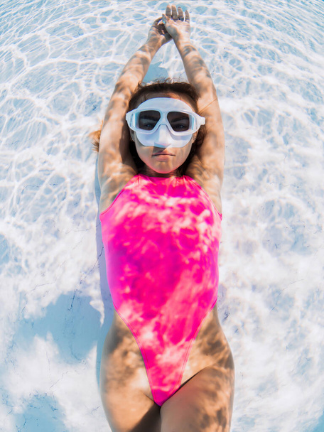Schöne Frau in rosa Badebekleidung mit Tauchermaske posiert unter Wasser im Pool. - Foto, Bild