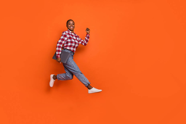 Full size portrait of active overjoyed lady rush fast hold wireless netbook isolated on orange color background. - Foto, Imagen