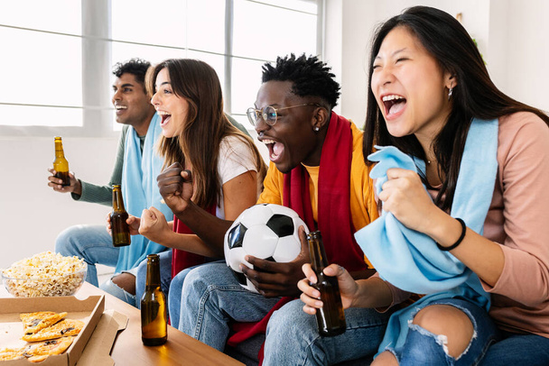 Wielu etnicznych młodych fanów piłki nożnej ludzi krzyczących i wspierających swoją drużynę narodową w meczu TV - Podekscytowana grupa różnorodnych przyjaciół bawiących się oglądając mecz piłki nożnej w telewizji - Koncepcja sportowa - Zdjęcie, obraz