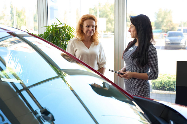 Cliente de un concesionario de automóviles se comunica con el interés de una joven gerente en el modelo de coche seleccionado - Foto, Imagen